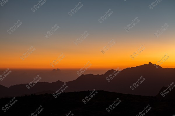 Sunset view over mountains, with the horizon lit in gradient orange and blue hues, as sunlight fades behind dark mountain peaks.