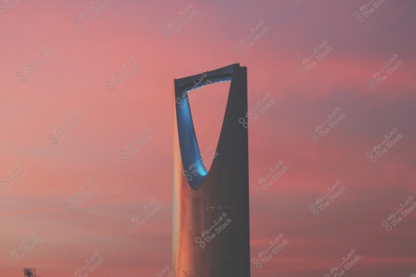 Image of the famous Kingdom Tower in Riyadh, Saudi Arabia, during sunset. The tower features a reflective glass facade, with the sky behind it painted in shades of pink and orange from the sunset.