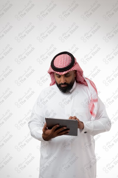 بورتريه رجل سعودي يحمل بيده الآيباد و ينظر لشاشته ويقوم بتعابير مختلفة، خلفية بيضاء