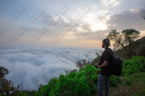 رجل سعودي واقف بجبل الأسود ممسك بالكاميرا يلتقط صورة الطبيعة في جازان