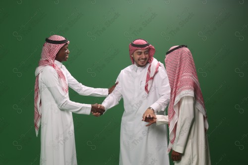 A young Saudi man in traditional Saudi dress shakes hands with his guests on an occasion