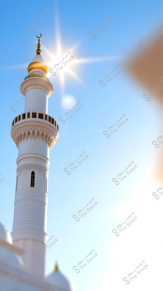 Image of a white mosque minaret topped with a golden crescent under a clear blue sky. Bright sunlight shines from behind the minaret, creating a beautiful light effect.