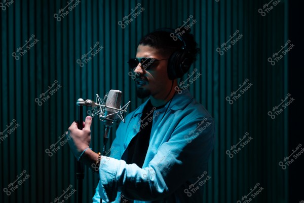 شخص يرتدي سماعات رأس ونظارات شمسية يغني في ميكروفون في استوديو تسجيل.