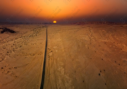 An overhead shot of a paved road that cuts through one of the Saudi deserts, showing the sky orange at sunset, nature in Saudi Arabia