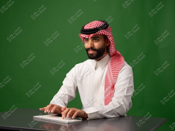 رجل يرتدي الثوب السعودي التقليدي ويعمل على جهاز كمبيوتر مع خلفية خضراء.