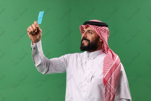 بورتريه رجل سعودي على خلفية خضراء مبتسم يحمل بطاقة الصرافة مستعد للتسوق