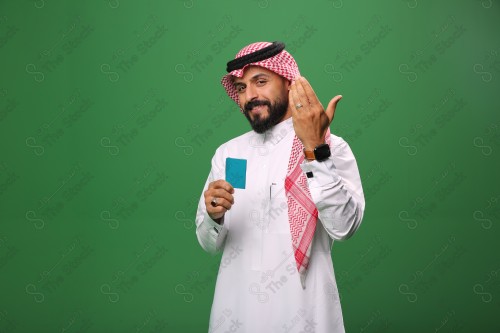 بورتريه رجل سعودي على خلفية خضراء متحمس يحمل بطاقة الصرافة مستعد للتسوق