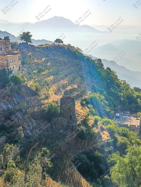 The image depicts a scenic mountain landscape with green agricultural terraces stretching across the slopes. A small village is situated on the edge of the mountain, with some stone houses integrated into the natural environment. In the background, mountains are shrouded in a light mist and the sky is clear, adding to the serene natural beauty of the scene.
