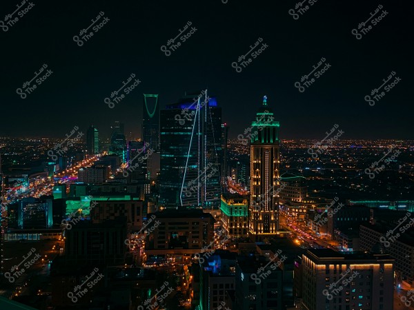 A night view of Riyadh city in Saudi Arabia, highlighting the Kingdom Tower and Al Faisaliah Tower illuminated with neon lights. Tall buildings spread across the horizon with streets lit by lamps.