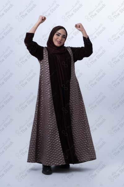 Portrait of a young Saudi woman wearing an abaya and hijab, with a smiling facial expression, standing against a white background