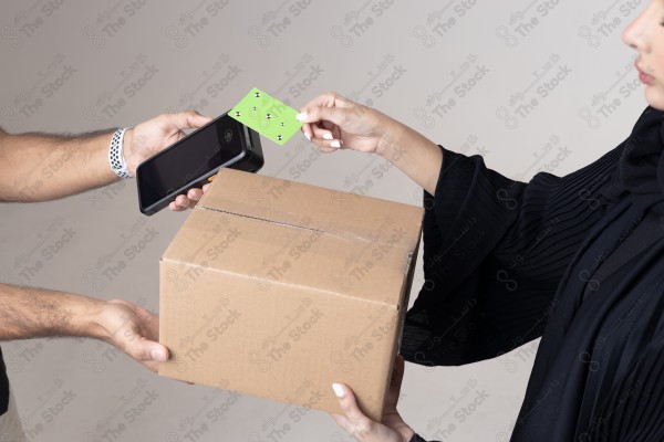 Portrait of a Saudi woman holding a card and making automatic payments, with a cardboard next to her on a white background