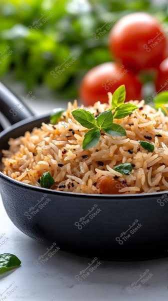 A photo of a seasoned rice dish in a deep black bowl, garnished with fresh basil leaves. In the background, ripe tomatoes and a blurred backdrop of green leaves are visible.