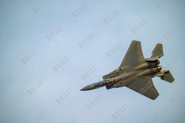 A jet fighter soaring in a slightly cloudy blue sky, showcasing its distinctive design with backward-swept wings and dual exhaust engines at the back. The aircraft is painted in camouflage colors.