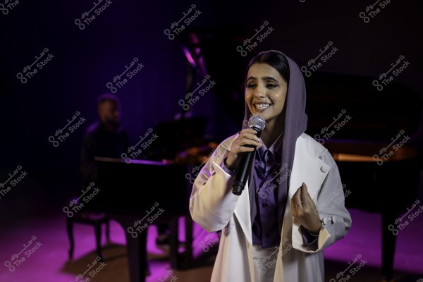 مغنية ترتدي وشاحًا بنفسجيًا وسترة بيضاء تغني في أداء حي مع عازف بيانو في الخلفية.