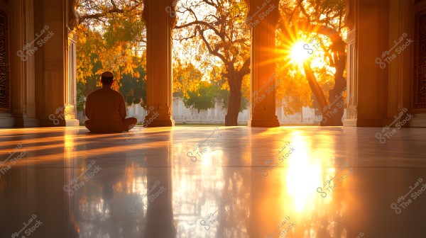 A person in traditional attire sits in an open space within an ornate building with columns, as sunlight filters through the trees outside, creating beautiful golden reflections on the glossy marble floor.