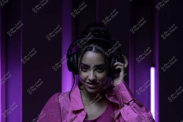 امرأة ترتدي سماعات كبيرة وتقف أمام خلفية أرجوانية.