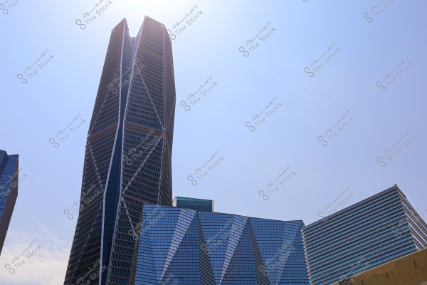An image of a high-rise building in an urban area, featuring a modern and unique architectural design. The building\'s exterior has prominent symmetrical lines, composed of glass and steel. The sky is clear and blue, reflecting light across the building surfaces.