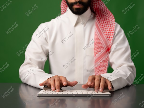 A man wearing a Saudi thobe and shemagh sitting in front of a keyboard.