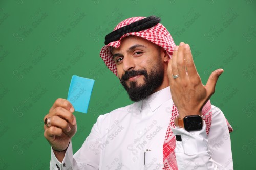 Portrait of an excited Saudi man on a green background, holding a debit card, ready to shop