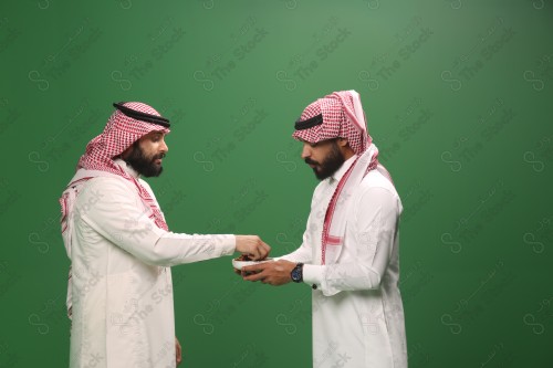 رجل سعودي يرتدي الزي السعودي التقليدي يقدم طبق من التمر لضيفه في أحد المناسبات