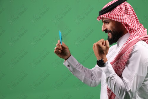 بورتريه رجل سعودي على خلفية خضراء متحمس يحمل بطاقة الصرافة مستعد للتسوق