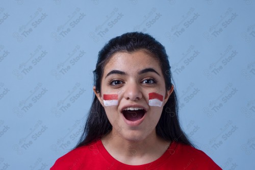 Portrait of a Saudi woman wearing a red T-shirt cheering the football team on a blue background and showing expressions of joy and enthusiasm, World Cup.