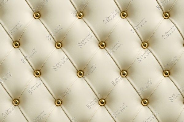 Image of a light-colored tufted fabric with shiny golden buttons evenly distributed. The design showcases a symmetrical geometric pattern, conveying a sense of luxury and elegance.