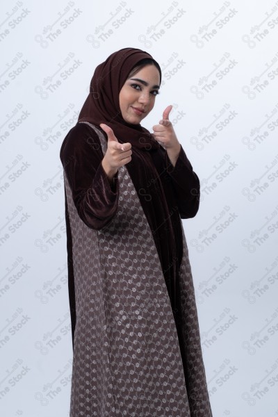 A young happy Saudi woman wearing an abaya, pointing her finger. Standing on white background.