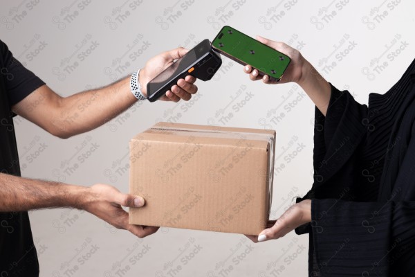 Portrait of a Saudi woman holding a card and making automatic payments, with a cardboard next to her on a white background