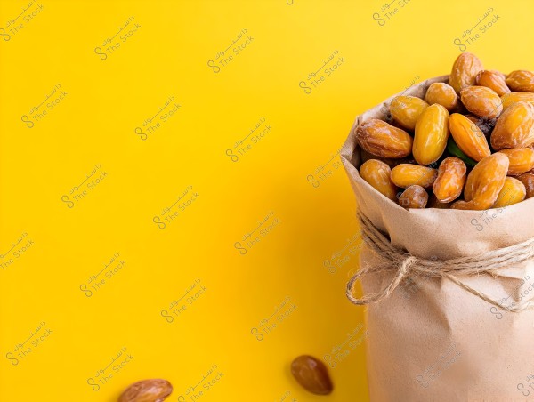 An image of a brown paper bag filled with fresh dates set against a bright yellow background. The bag is tied with a string around its neck. A few dates are scattered beside the bag.