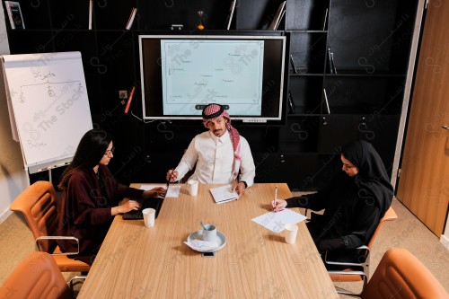 A Saudi man in traditional Saudi dress holds a meeting with Saudi female employees wearing abaya in the meeting room