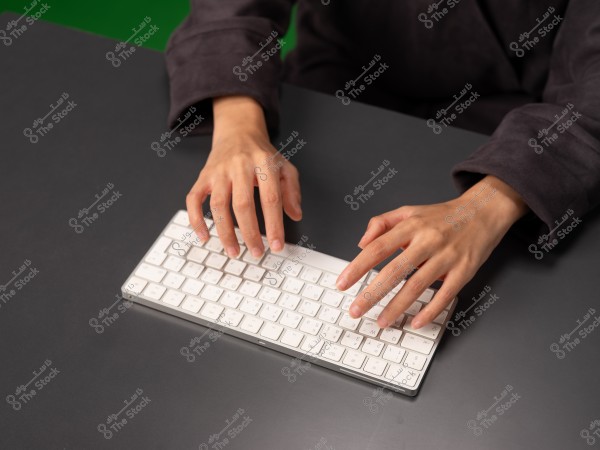 Hands typing on a white keyboard placed on a gray table surface.