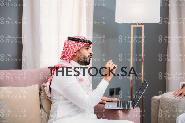 رجل سعودي يرتدي الثوب و الشماغ، يتحدث وهو يمسك بلكمبيوتر المحمول