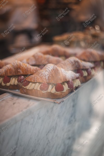 Croissant filled with cream and topped with red raspberries and powdered sugar on a marble table.