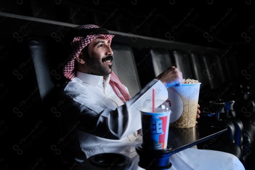 شاب سعودي يرتدي الزي السعودي التقليدي يشاهد أحد الأفلام المعروضة بينما يتناول من الفشار