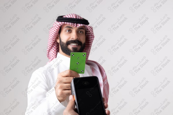 Portrait of a Saudi man holding a card and making automatic payments on a white background