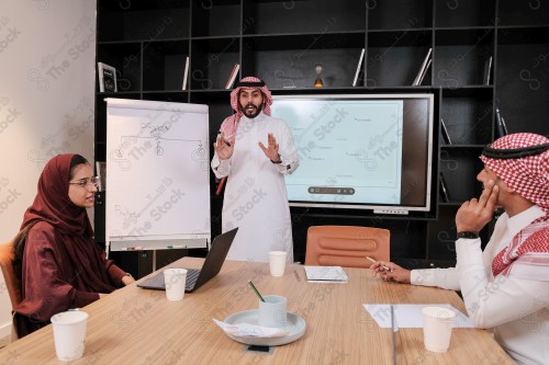 A Saudi man in traditional Saudi dress conducts a business meeting in the boardroom during the day