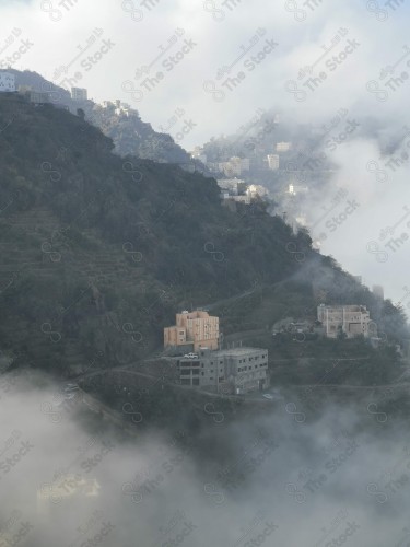 A phone shot showing a group of houses and forests showing clouds embracing it  in the Fayfa governorate in the Jazan region in southern Saudi Arabia.