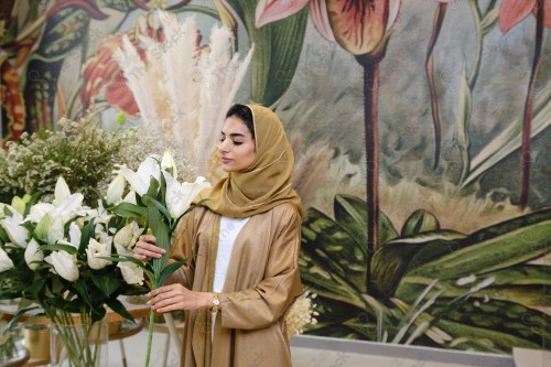 A Saudi woman wearing an abaya working in a flower shop, a bouquet of roses. Holidays and occasions, happy occasions, surprise, Christmas