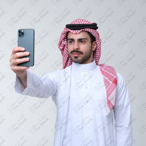 بورتريه رجل سعودي يرتدي الثوب يبتسم وهو يلتقط سيلفي بجواله