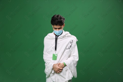 Portrait of a pilgrim with white skin on a green background, wearing Ihram to perform Hajj, performing the duty of prayer