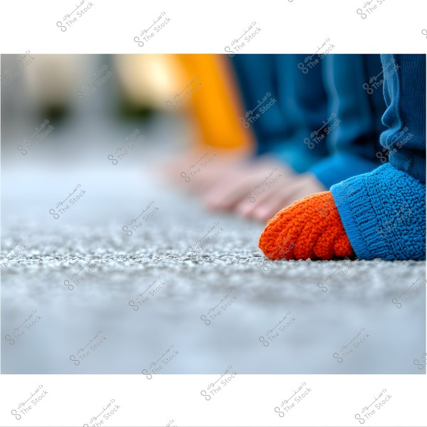 Image showing several hands placed on a textured grey carpet. The right hand is wearing an orange glove with a blue sleeve, while the other hands are bare and wearing blue clothing. The composition suggests a moment related to prayer or meditation.