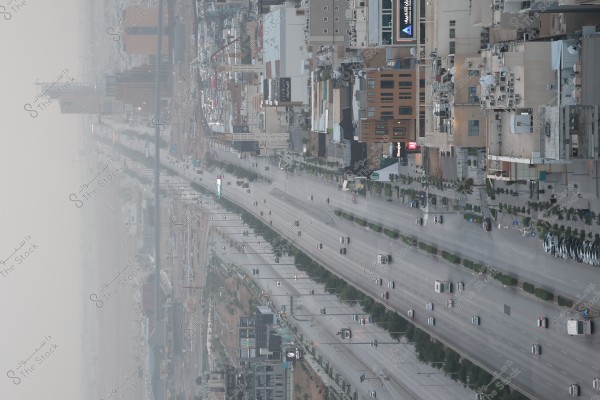 An image showing a wide street in an urban city with multiple vehicles moving and parked along the road. Modern buildings are situated on both sides, with some commercial signs visible. The air appears slightly hazy, creating a muted background in the image.