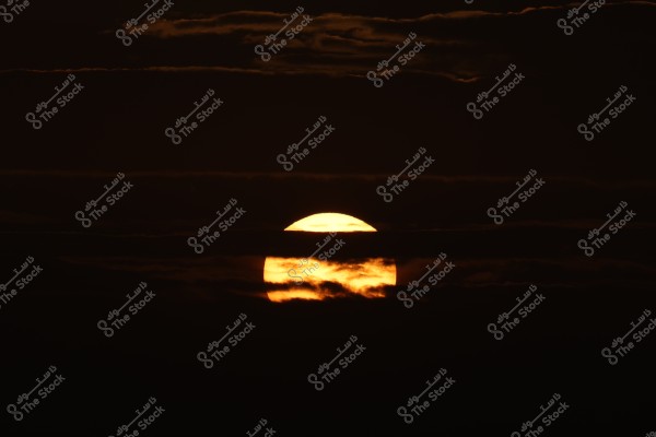 An image showing a sunset with the sun disc glowing orange amidst dark clouds in the sky, creating a dramatic and serene scene at the end of the day.