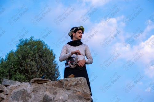 A Saudi man wearing a traditional dress at the top of the mountain and behind him clouds appear in Jizan