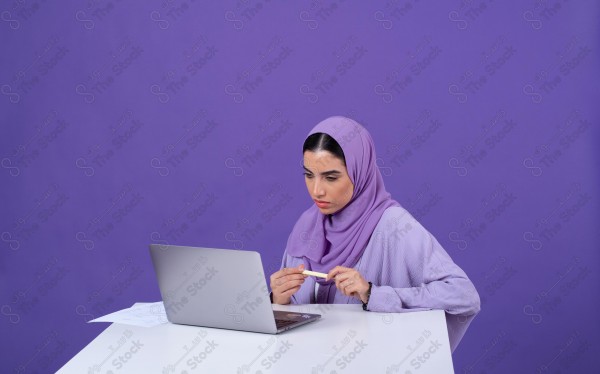 Portrait of a young Saudi woman wearing an abaya and hijab, holding a pen and thinking, against a purple background