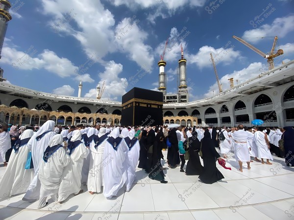 A group of pilgrims circumambulating the Kaaba in the Grand Mosque in Mecca under a clear sky.