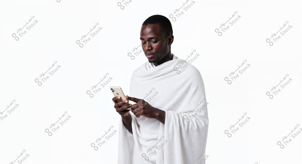 صورة لرجل يرتدي إحرام أبيض, وهو ممسك بهاتف ذكي وينظر إليه. الخلفية بيضاء تماماً, مما يبرز تفاصيل اللباس التقليدي المستخدم في مناسك الحج أو العمرة في المملكة العربية السعودية.