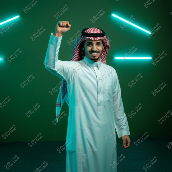 A portrait of a man wearing a white thobe and a traditional red and white headdress in front of a green background with bright blue lighting lines. The man raises his right hand in a celebratory gesture and smiles warmly. The clothing is likely of Saudi origin.