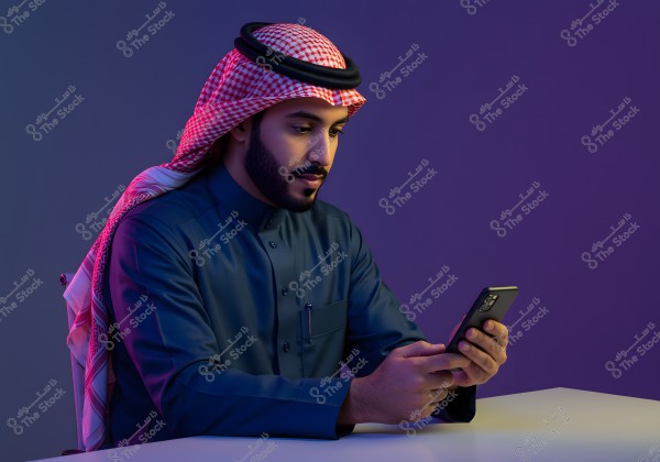 A portrait of a man wearing traditional Saudi attire with a dark blue thobe and a red and white checkered keffiyeh with a black agal. The man is sitting at a desk using a smartphone, with a softly lit purple background.